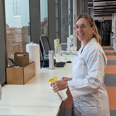 Female researcher in laboratory holding spray bottle and smiling at camera. Image, UQ